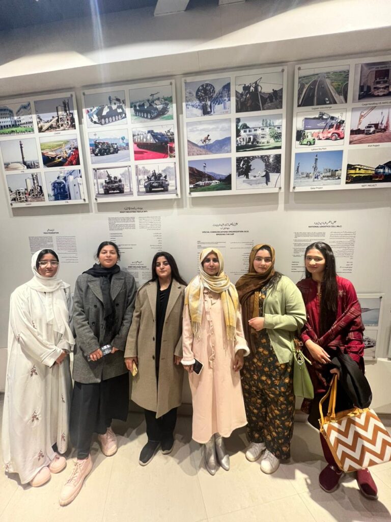 Female students with Dr. Saniya Moazzam engaging in experiential learning in front of military equipment displays.